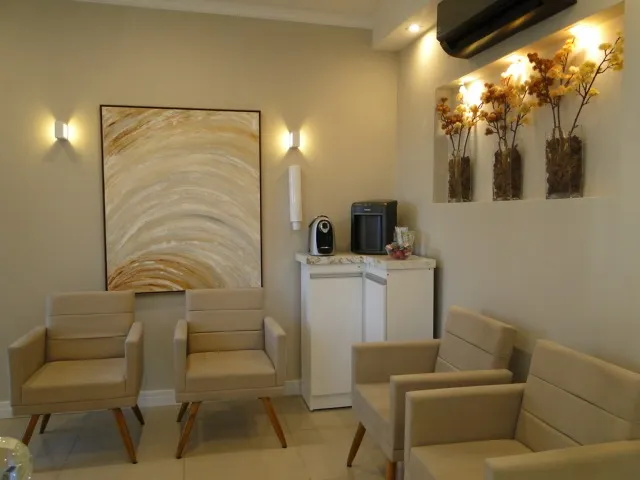 Recepção da clínica com poltronas bege e nicho com flores secas